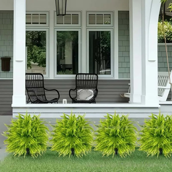 Two artificial green fern stakes planted in a lawn in front of a gray house