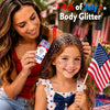Une jeune fille applique du body glitter dans ses cheveux tandis qu'une femme sourit en arrière-plan.