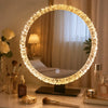 A round, illuminated vanity mirror with a textured glass frame sits on a dark base next to makeup brushes and skincare produc