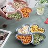 A heart-shaped four-compartment snack tray filled with various nuts, seeds, and dried fruits.