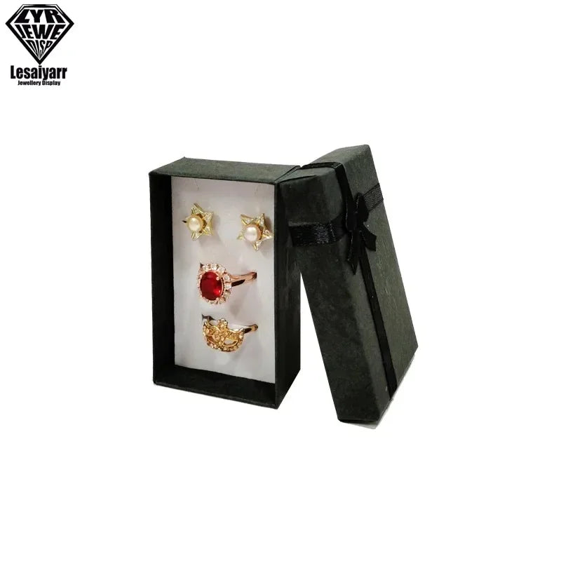 Caja de regalo decorativa negra con tapa abierta, mostrando dos pequeños aretes dorados.