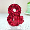 A red glitter number eight candle decorated with a large red bow for a birthday or celebration.