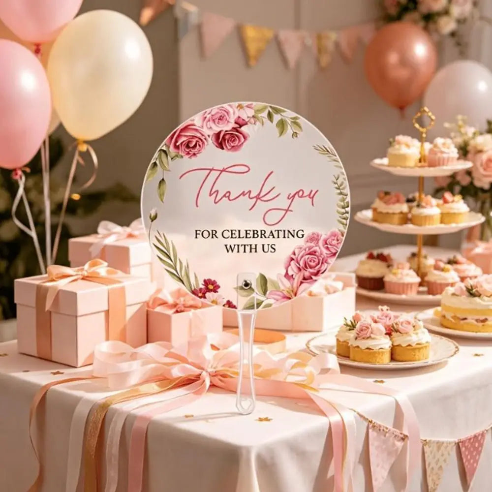 A display of pink floral thank you hand fans and gift boxes on a white table with pink ribbon accents.
