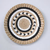 Round woven straw wall decor hanging with concentric black and white patterns.