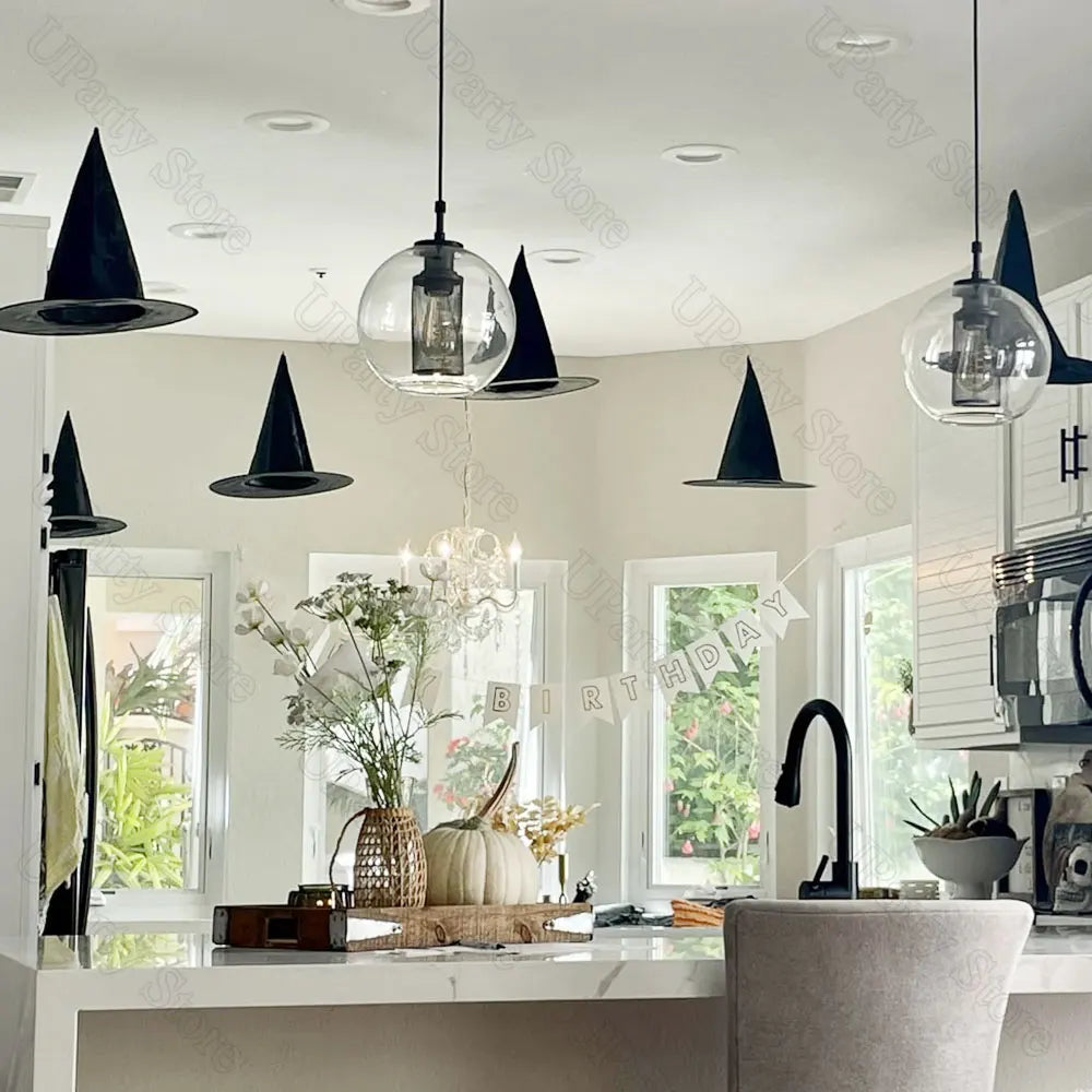 Classic black witch hats with hanging rope used as Halloween décor displayed above a kitchen counter.