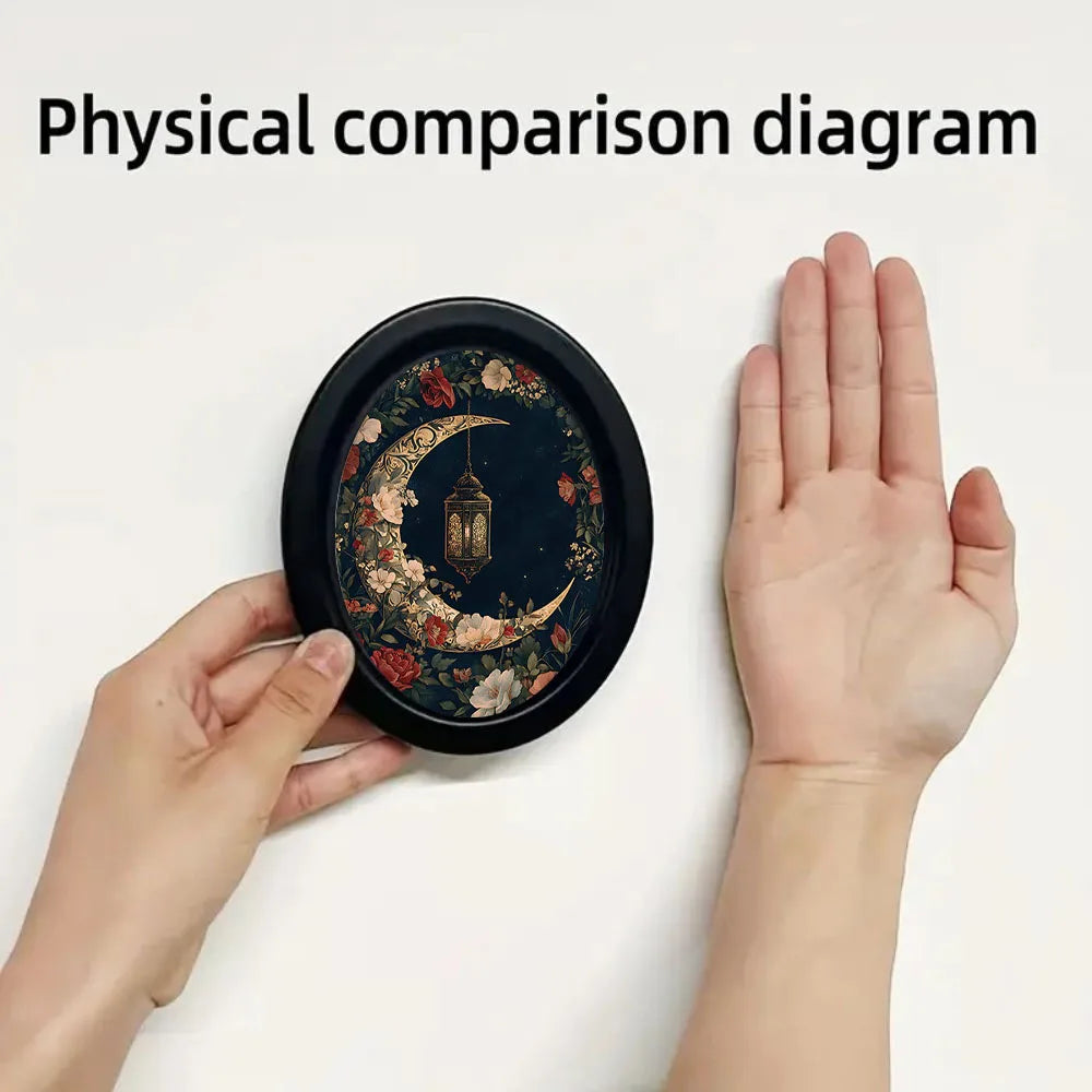 A hand holds a circular piece of dark wall art featuring a crescent moon and ornate lantern design.