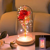 An LED galaxy rose artificial flower displayed inside a glass dome on a wooden base.