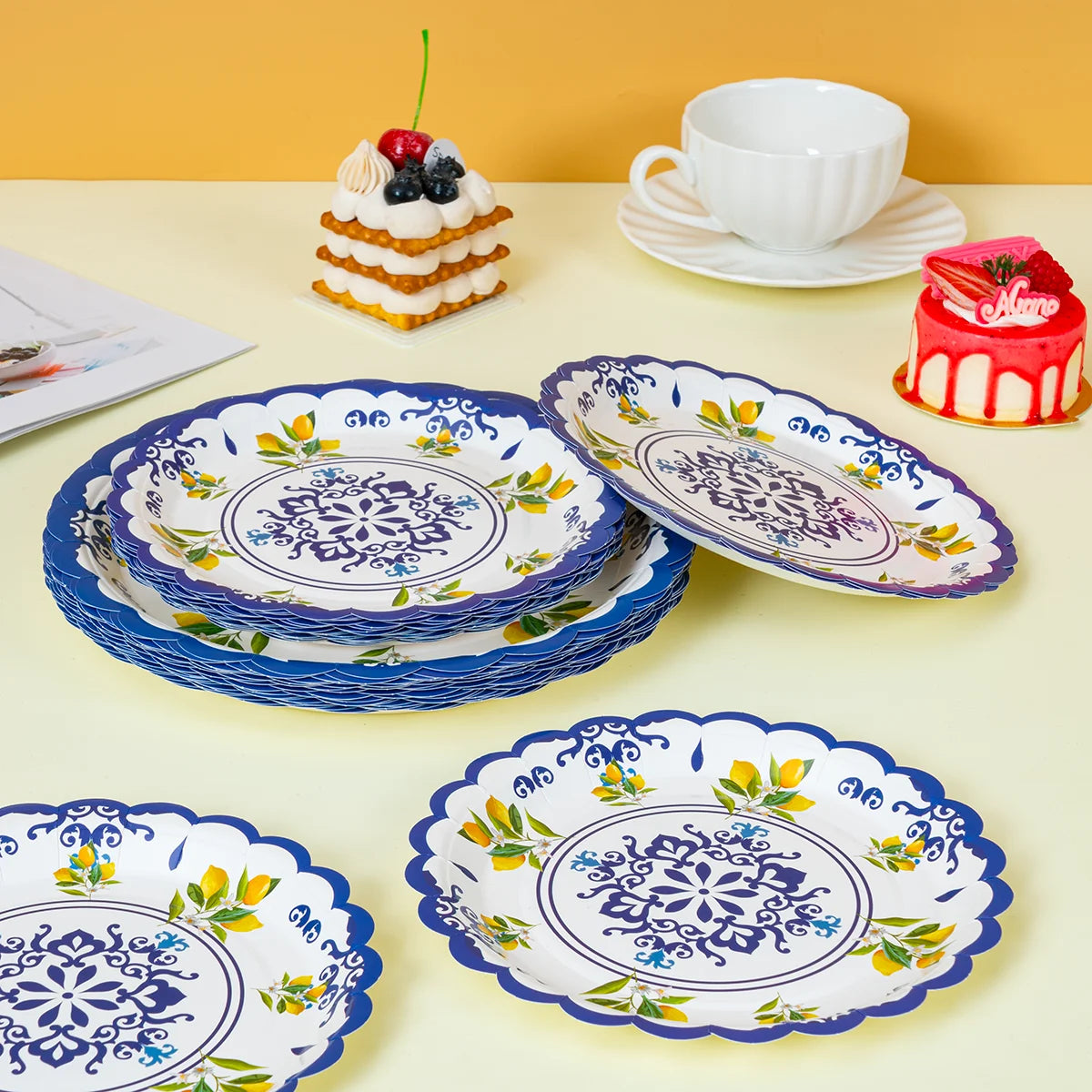 A stack of blue floral paper plates and a plate with a red cake are displayed on a light yellow surface.