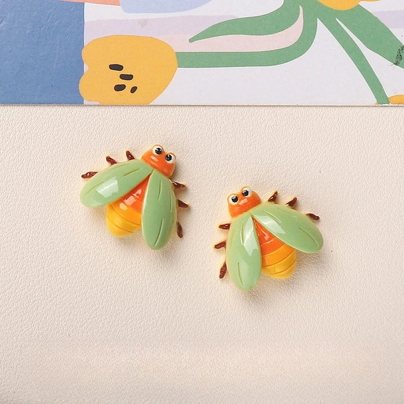 Two small resin insect magnets featuring orange and green butterfly or bee designs against a light background.