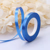 A roll of blue satin balloon ribbon unwinding on a white surface amidst light beige petals.
