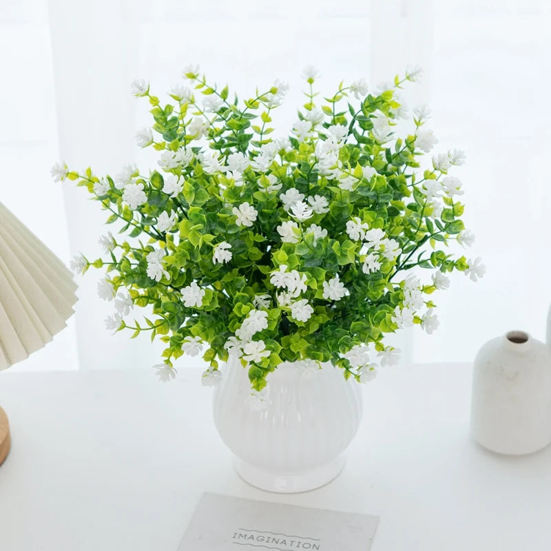 A bouquet of artificial eucalyptus branches with green leaves and white flowers in a white vase.