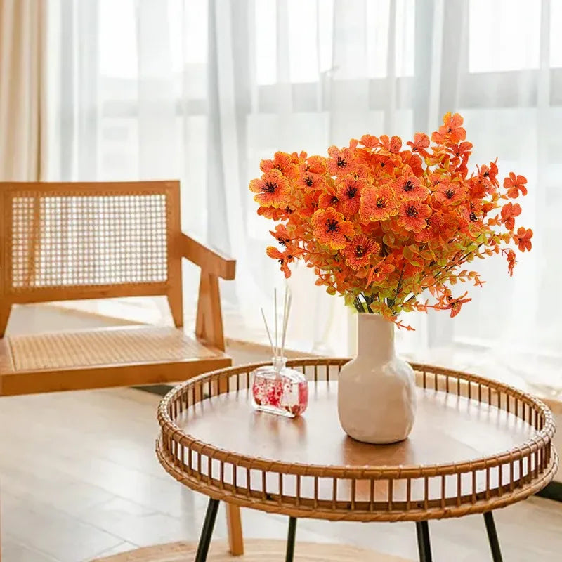 An artificial autumn bouquet of vibrant orange and yellow silk flowers displayed in a white vase on a wooden table.
