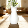 A white cat-shaped table vase with large eyes sits on a light brown rug in a sunlit living room.