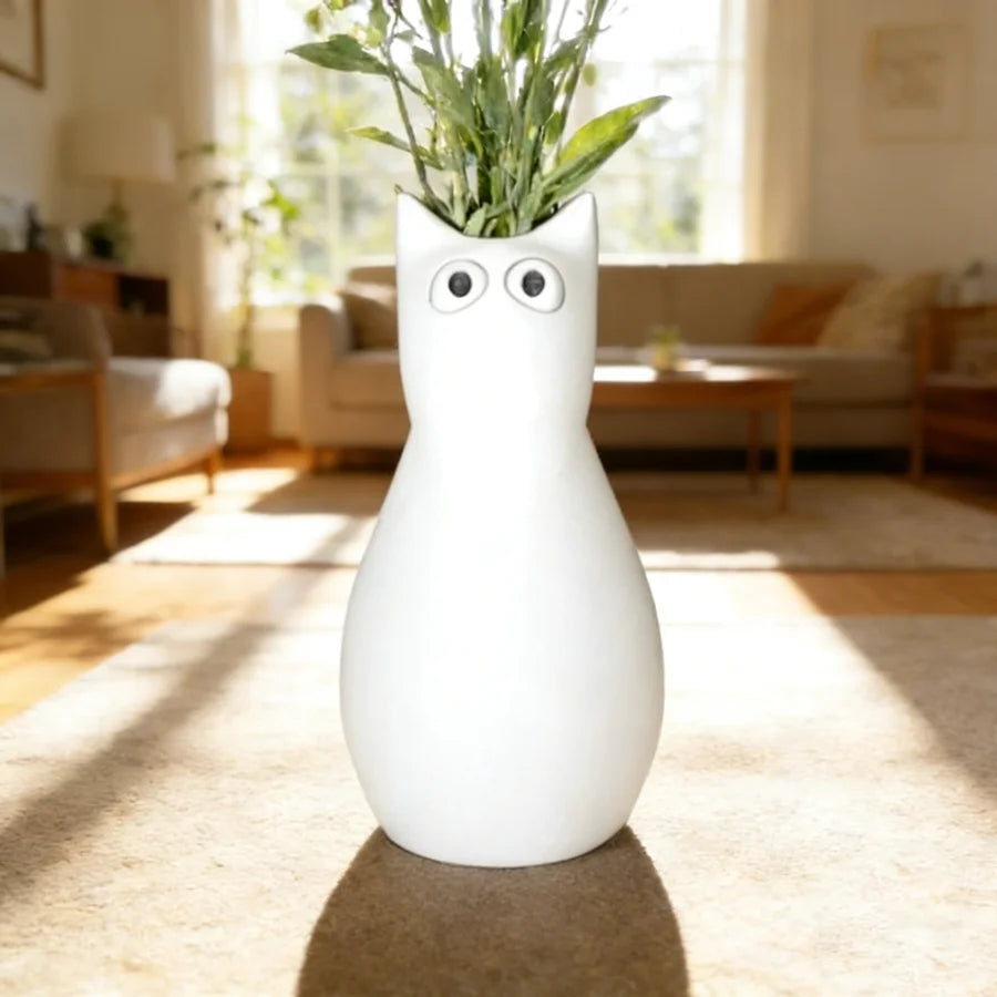A white cat-shaped table vase with large eyes sits on a light brown rug in a sunlit living room.