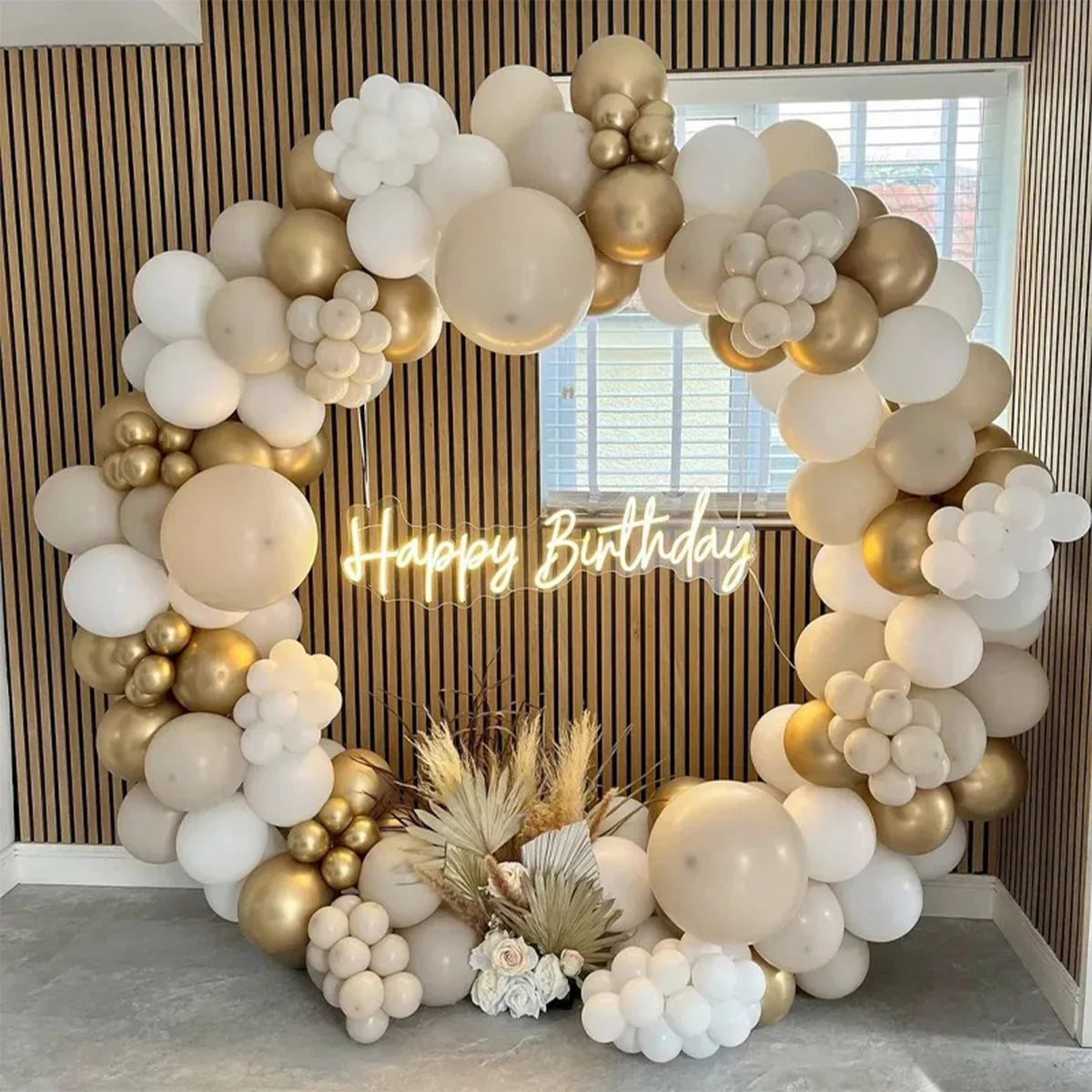 A large balloon garland arch made of white and beige latex balloons decorated with dried grasses and flowers.