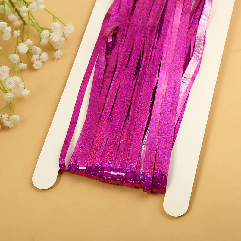 A vibrant magenta metallic tinsel foil fringe curtain backdrop displayed on a white hanger against a beige background.