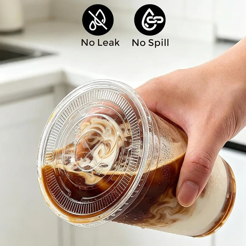 A hand holds a clear plastic cup with a lid containing iced coffee and whipped cream.