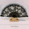 Black and gold lace folding fan with a rose pattern displayed on a wooden stand.