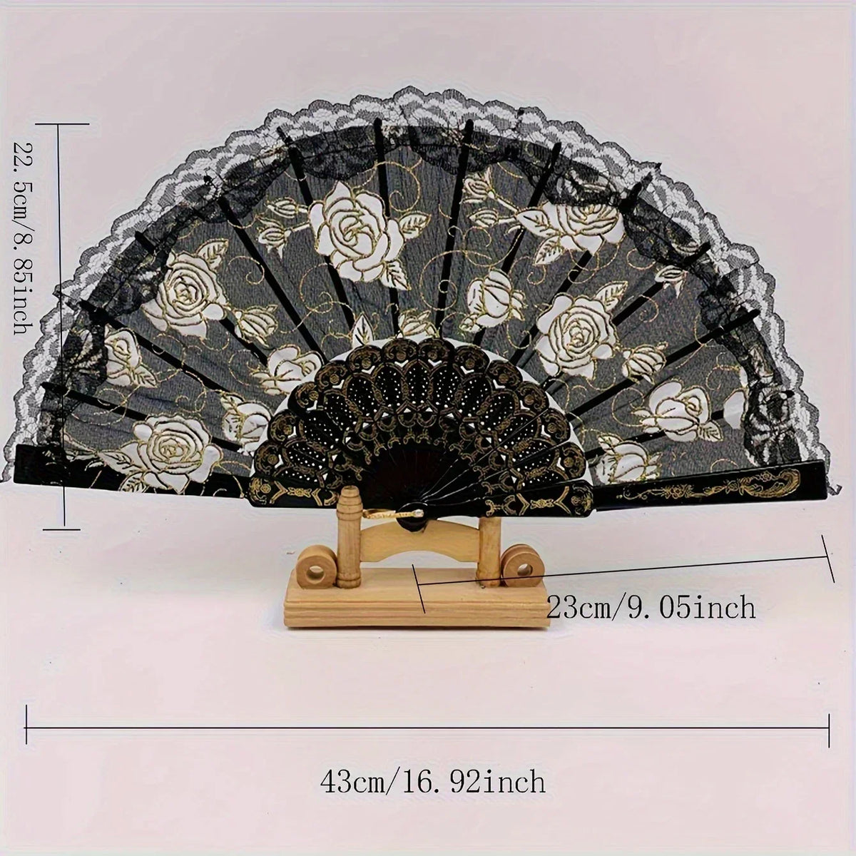 Black and gold lace folding fan with a rose pattern displayed on a wooden stand.