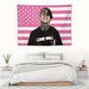 A tapestry featuring a pink and white American flag design with a man's face in the center.