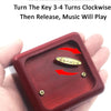 A hand holds a red wooden clockwork music box with a key and a small golden piece.