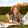 A smiling girl holds a reusable plastic dessert cup with a spoon outdoors on a blanket.
