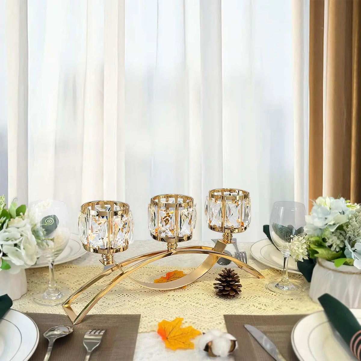 A three-arm gold crystal candelabra displayed on a table with white linens and floral arrangements.