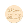 A round wooden sign with gold lettering that reads Welcome to the world little one