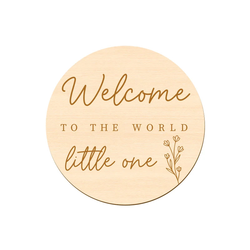A round wooden sign with gold lettering that reads Welcome to the world little one