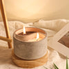 A round gray silicone mold for a DIY candlestick holder sits on a wooden base with a lit candle inside.