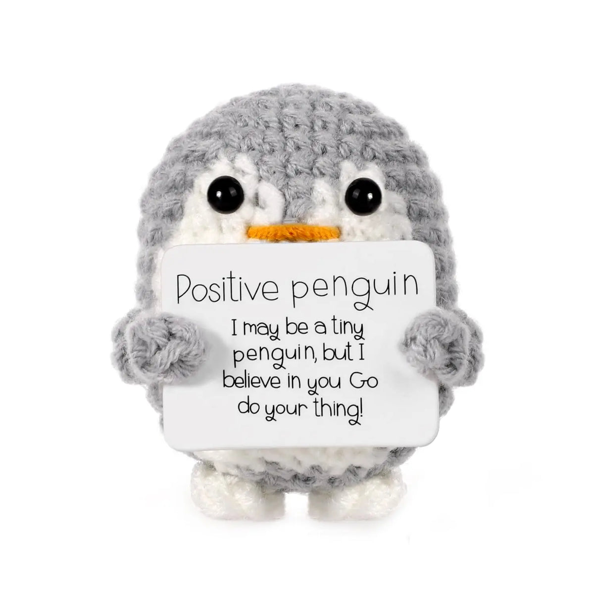 A gray crocheted penguin plush holding a white card with the text Positive penguin I may be a tiny penguin but I believe in y