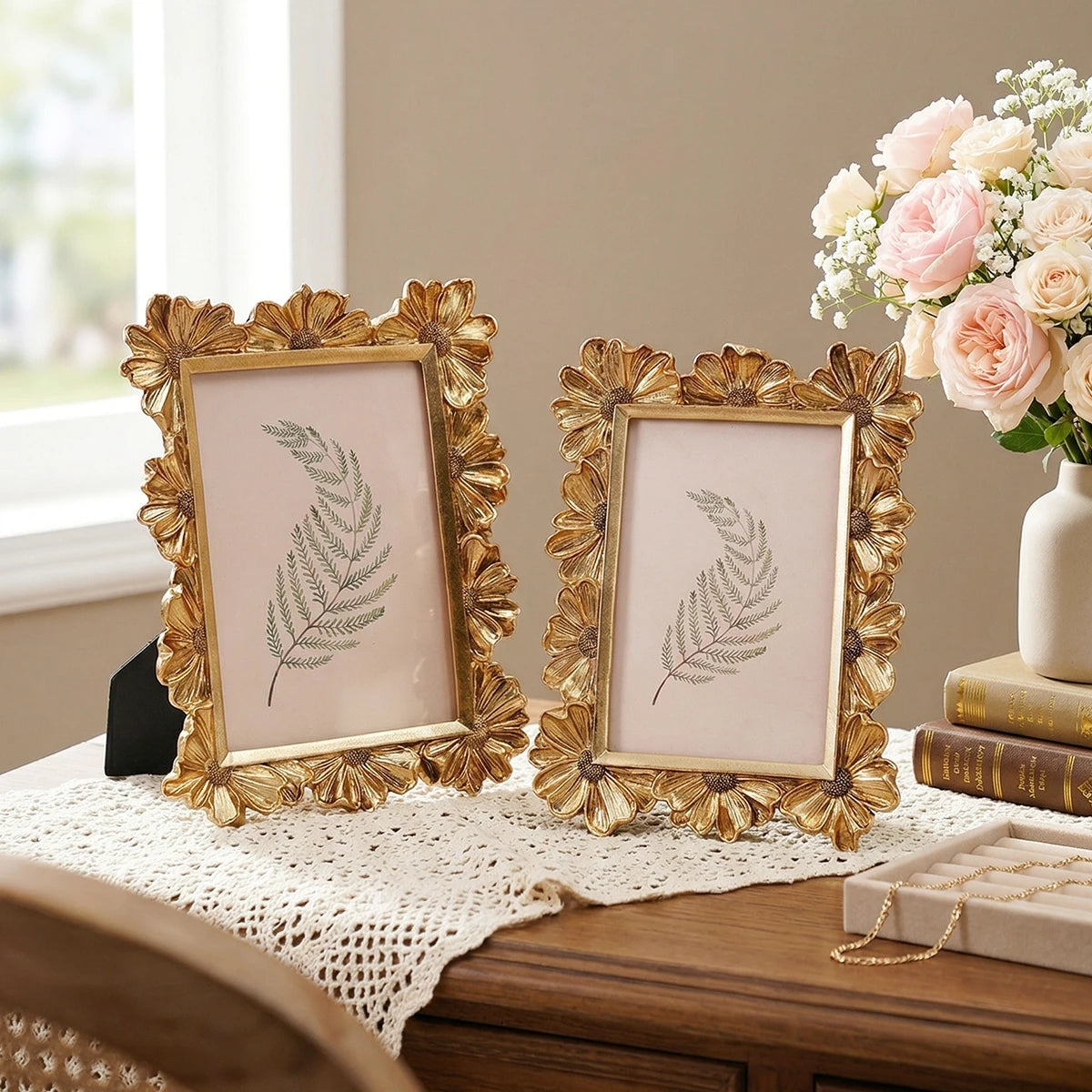 Two ornate golden resin photo frames with natural greenery designs displayed on a wooden surface.