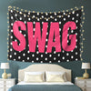 A pink polka dot tapestry with the word SWAG displayed on a dark background, hanging above a bed.