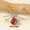 A Red Jasper crystal spider figurine resting on a light background next to a wooden stick.