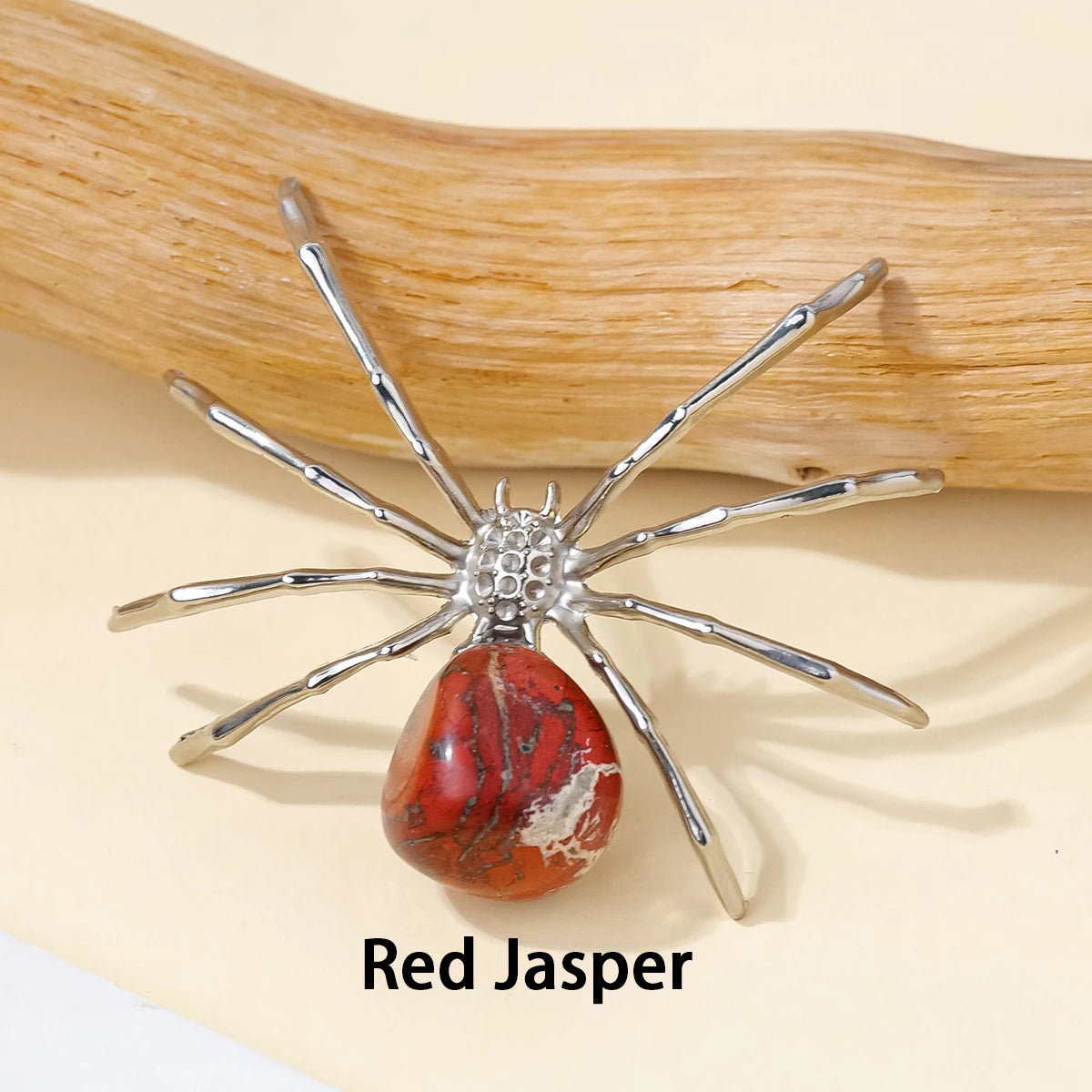 A Red Jasper crystal spider figurine resting on a light background next to a wooden stick.