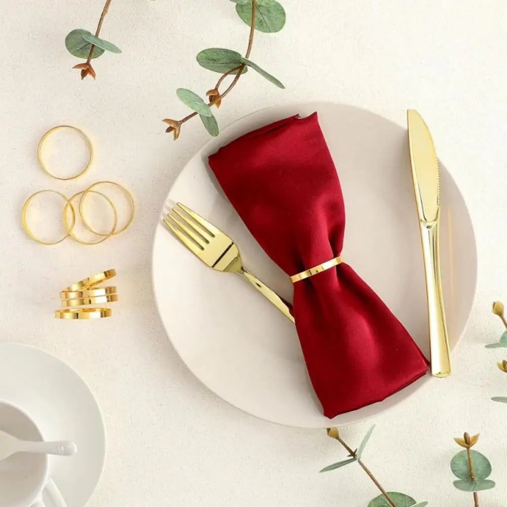 Ein Teller mit einem tiefroten Satinserviette, gebunden mit einem goldenen Ring, sowie einer goldenen Gabel und Messer.