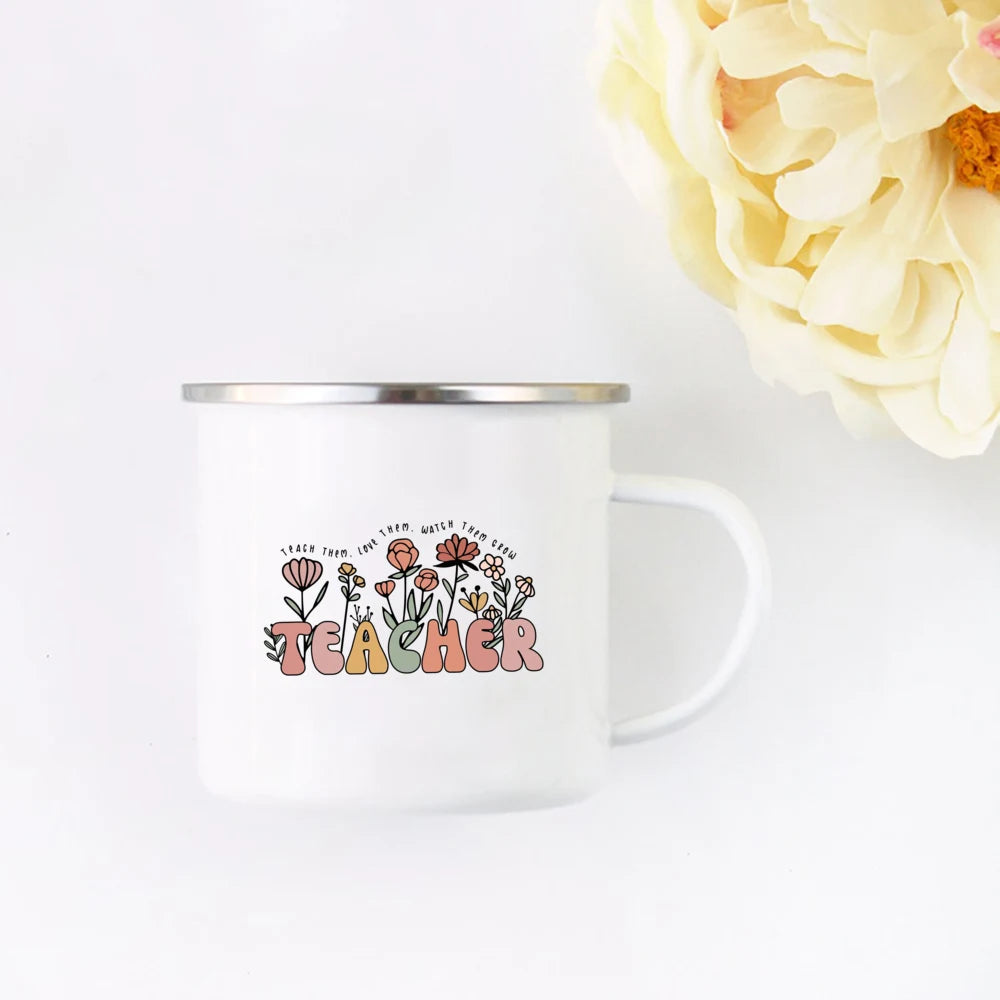 A white enamel mug with a floral design and the word TEACHER printed on it, set against a white background.