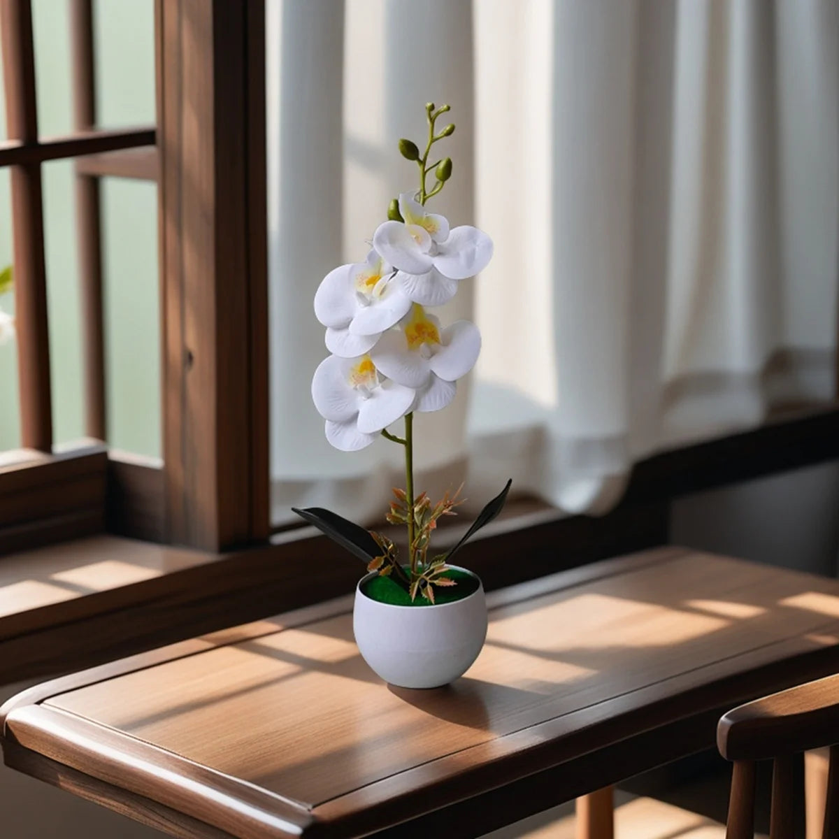 A white artificial orchid plant in a small pot sits on a wooden table next to a window.