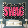 A pink polka dot tapestry with the word SWAG displayed on a dark background hanging above a bed.
