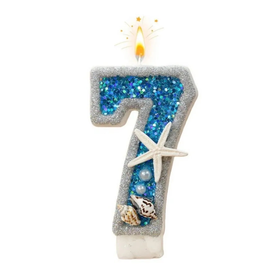 A number seven candle decorated with blue glitter and starfish accents.