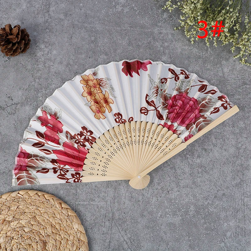 A hand carved bamboo folding fan with pink and red floral patterns displayed on a gray surface.