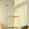 A light wood macrame floating wall shelf with a hanging rope is mounted on a pale wall.