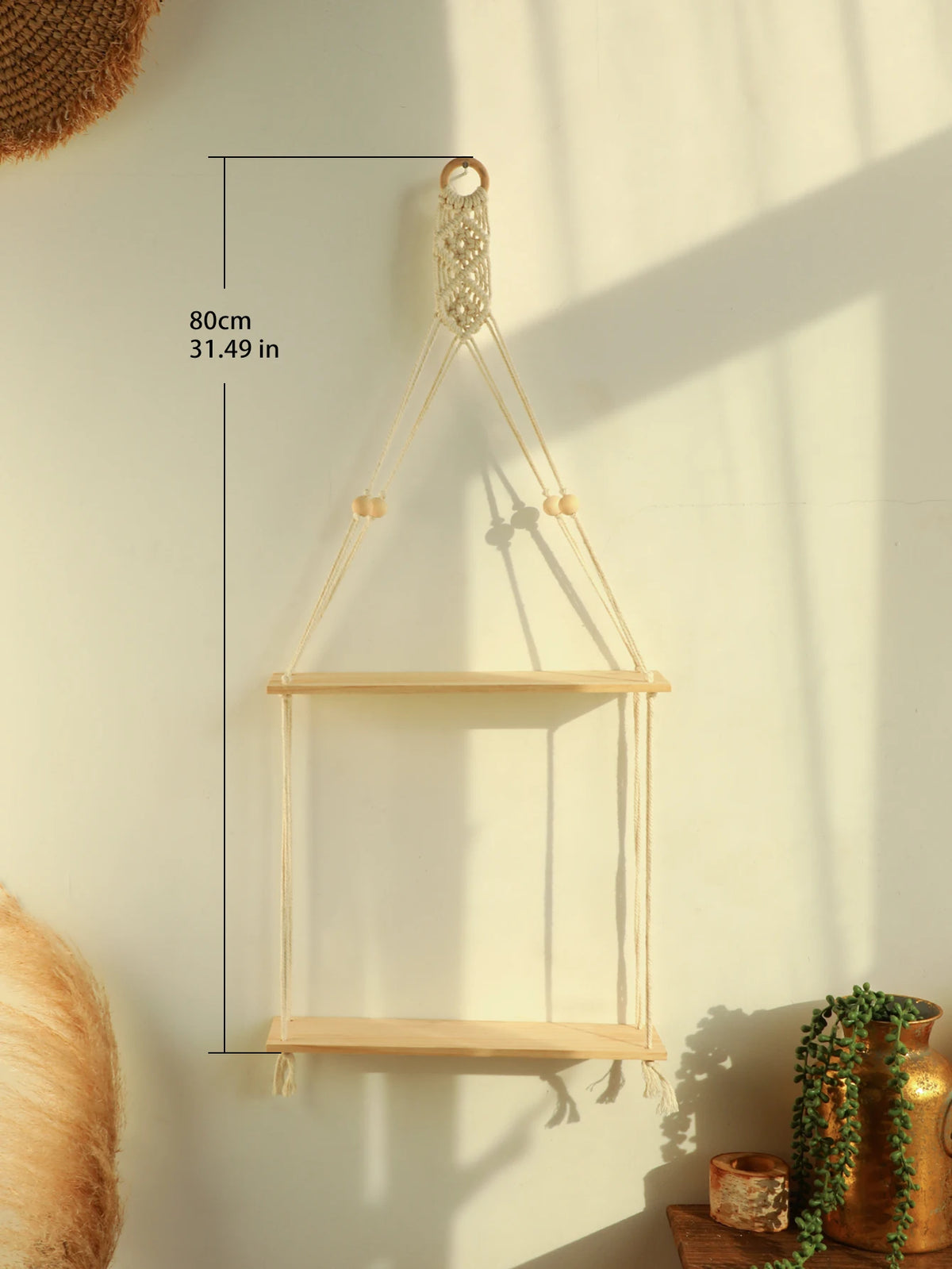 A light wood macrame floating wall shelf with a hanging rope is mounted on a pale wall.