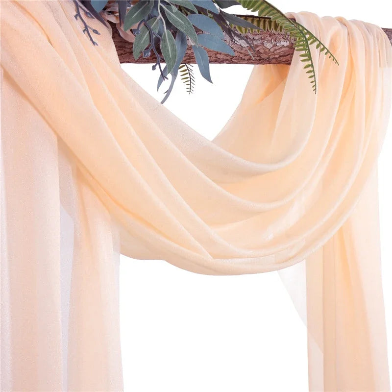 Light peach chiffon fabric panels draped over a wooden arch with green foliage.