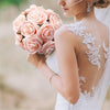 A bride holds a bouquet of soft pink artificial roses with a lace-detailed back on her wedding dress.