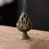 A vintage alloy incense burner holder with a textured, flame-like design emitting smoke on a wooden surface.