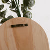 Jarrón de pared arqueado de madera clara con soporte metálico oscuro y hojas de eucalipto verde.