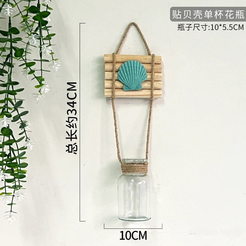 A decorative glass terrarium featuring a wooden plant holder with a blue seashell and a natural twine hanger.