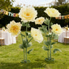 Large artificial silk yellow poppy flowers on green stems displayed in a stand on a grassy lawn.