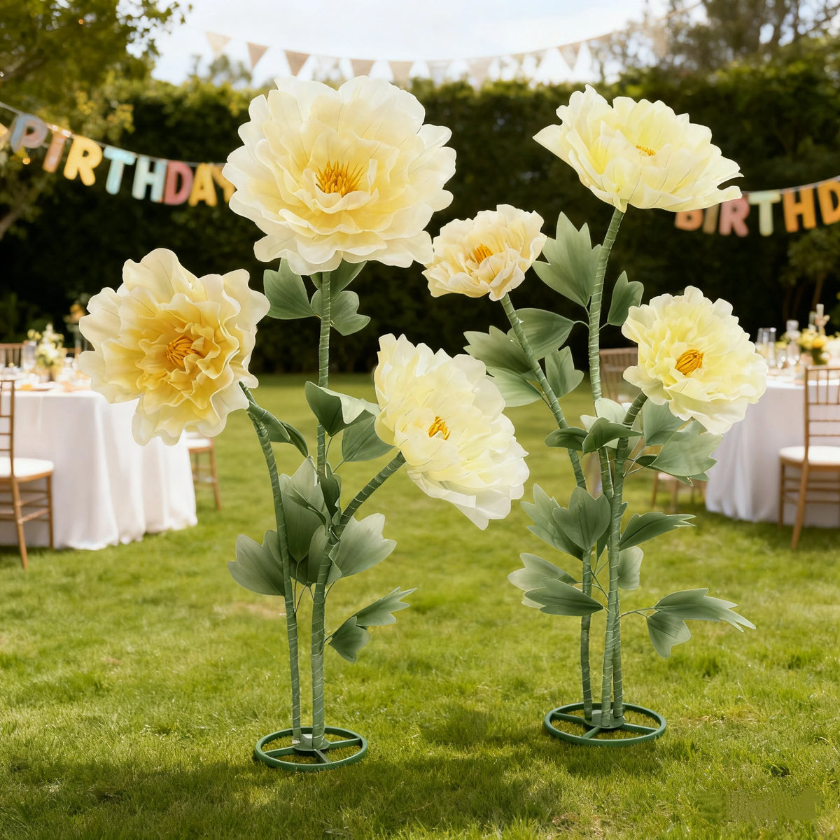 Large artificial silk yellow poppy flowers on green stems displayed in a stand on a grassy lawn.